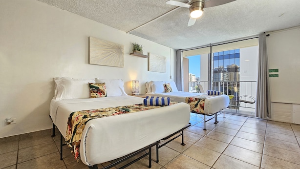 A hotel room with a bed, a desk, and a chair. There is a balcony with a view of the city. - 2 Queen Beds & a Pool in Waikiki +FREE Parking! (Honolulu)