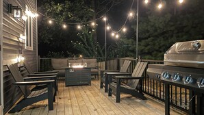 Un patio al aire libre con una parrilla, asientos e iluminación con guirnaldas.