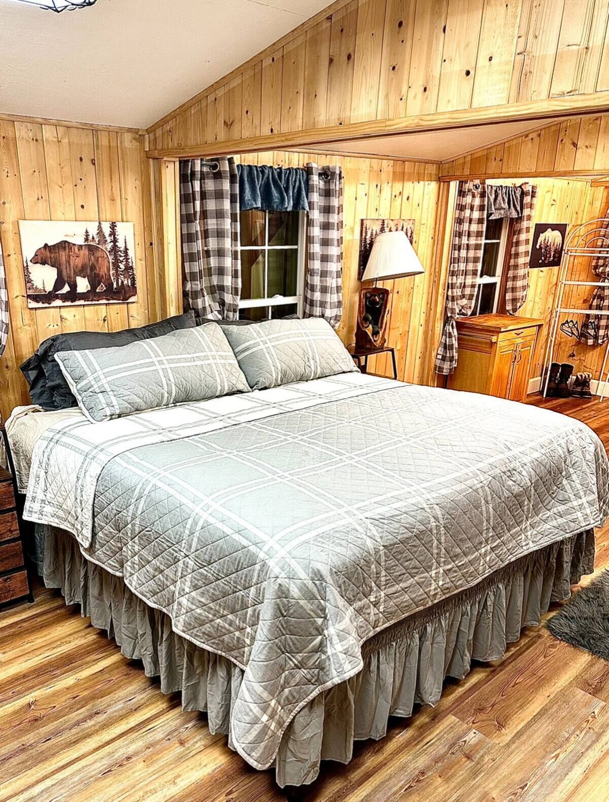 A wooden-paneled bedroom with a large bed, plaid curtains, and a bear-themed wall art.