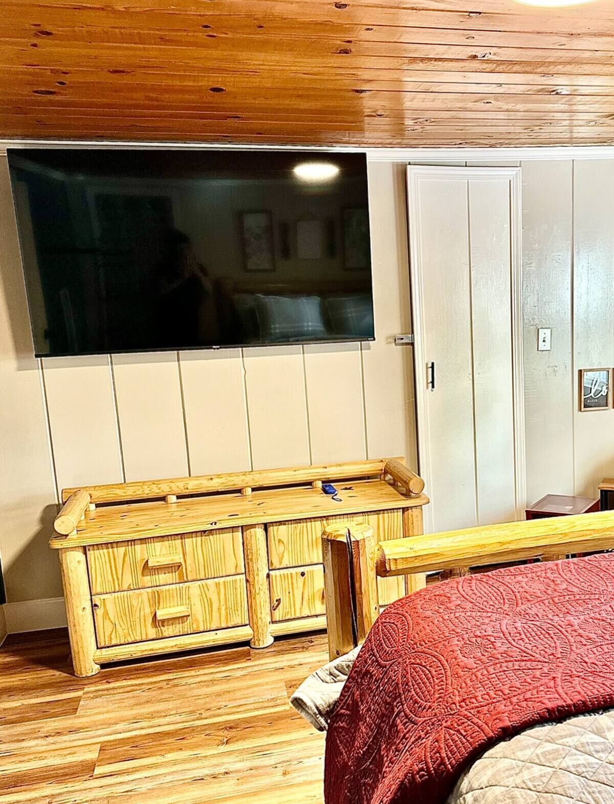Une pièce avec un meuble en bois, une grande fenêtre et un lit recouvert d’une couverture rouge.