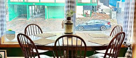 Un coin repas comprenant une table et quatre chaises, un ventilateur de plafond et une vue sur une rue bordée d’immeubles et de voitures garées.