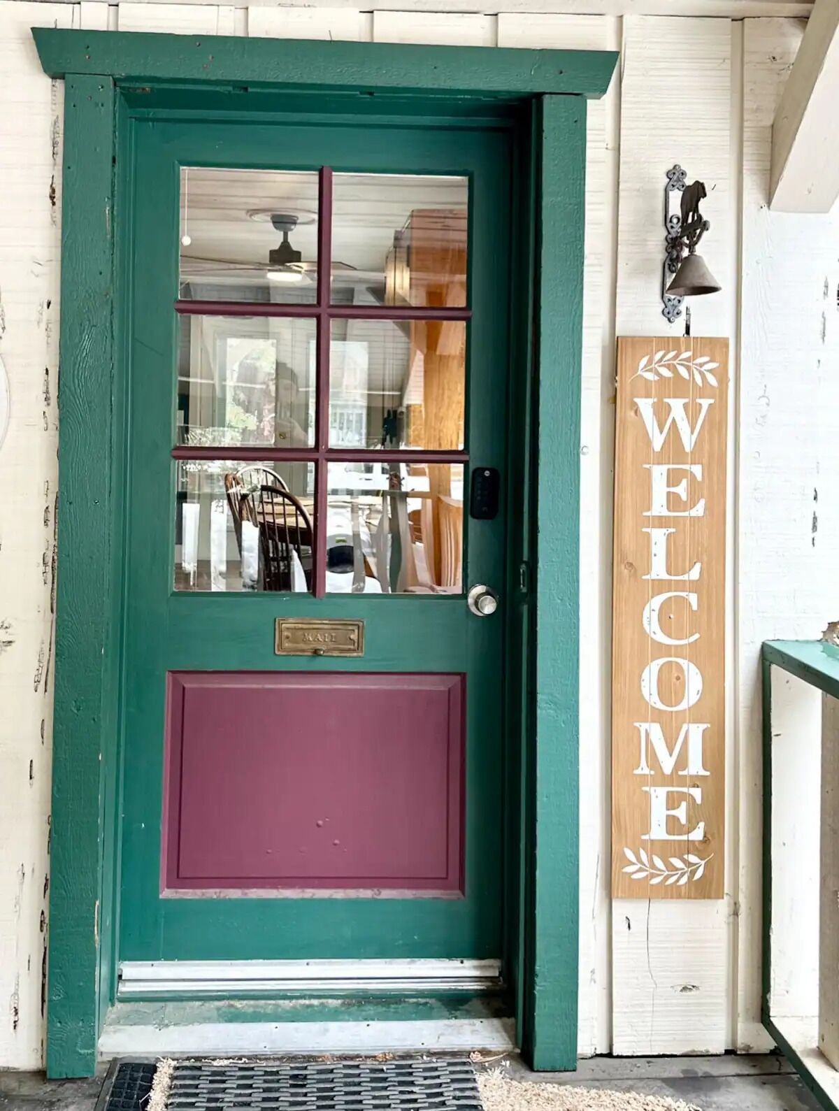 Une porte verte avec une fenêtre, une boîte aux lettres et une pancarte indiquant « BIENVENUE ».