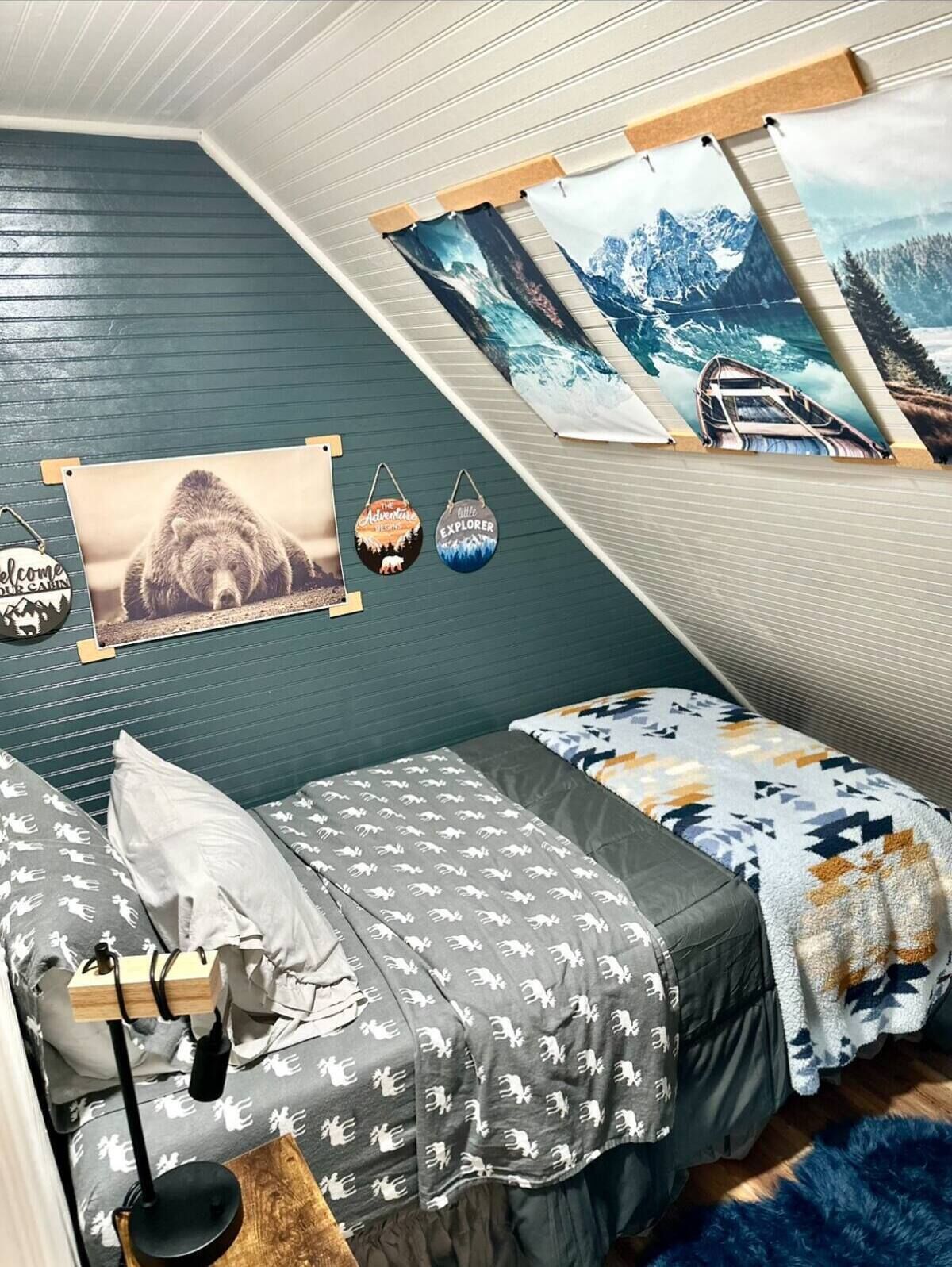 A cozy attic bedroom with two beds, a wooden desk, and a large window.