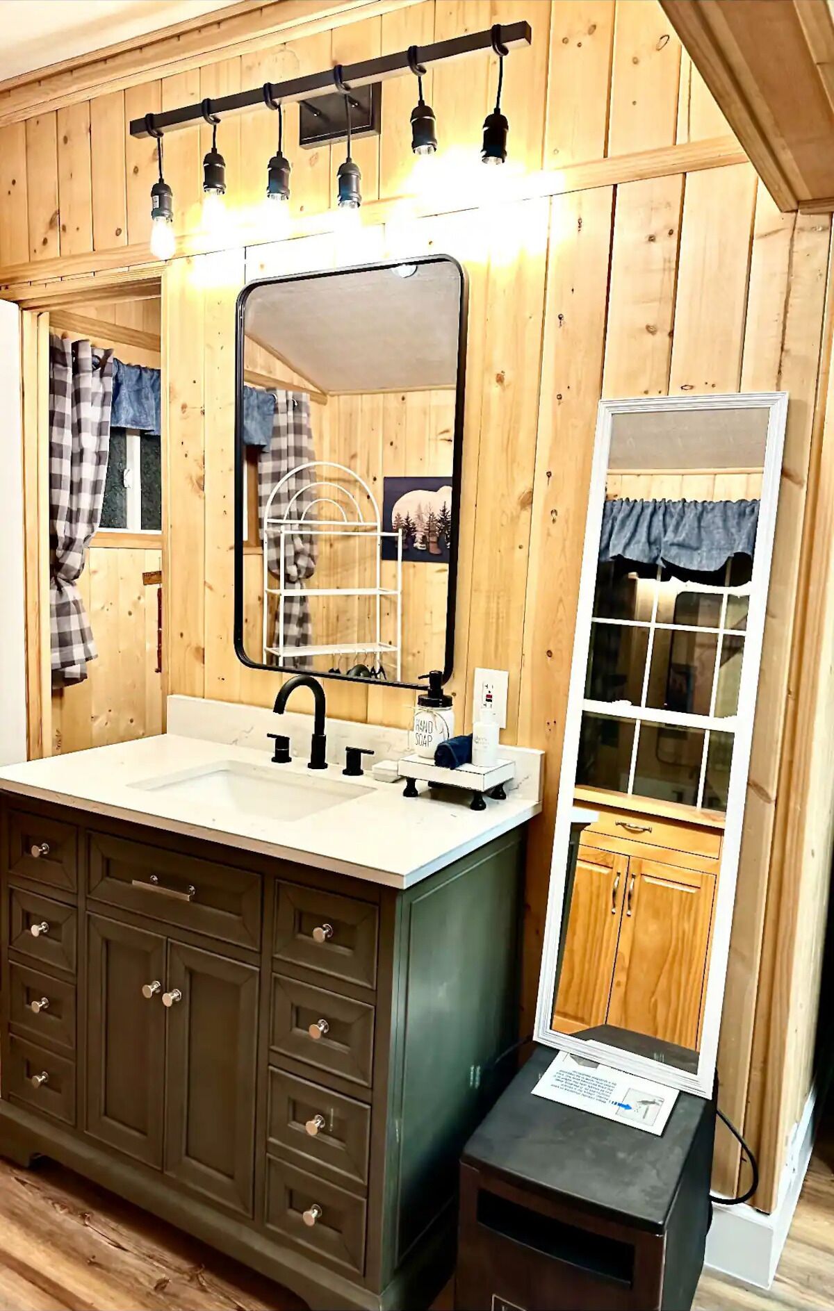 A bathroom with wooden paneling, a large mirror, a sink with a black faucet, and a vanity with multiple drawers.