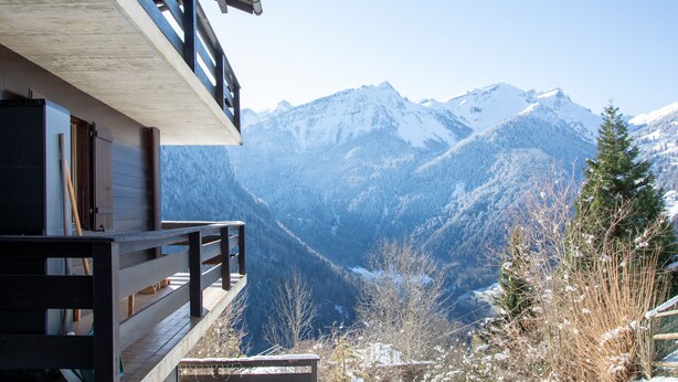 A wooden cabin with a balcony overlooking a mountainous landscape.
