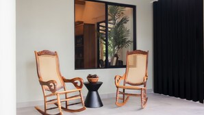 A room with two rocking chairs, a small table with a potted plant, and a large window with a view of a plant outside. - Palma Verde Arenal (La Fortuna)