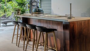 A modern kitchen with a wooden island, bar stools, and a view of a lush garden. - Palma Verde Arenal (La Fortuna)