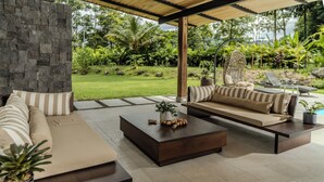A modern outdoor living area with a stone wall, a sofa set, a coffee table, and a hanging chair. - Palma Verde Arenal (La Fortuna)