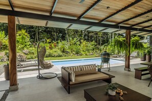 Un espace extérieur abrité comprenant une piscine, un canapé et diverses plantes.