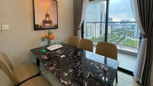 A modern dining area with a marble table, chairs, a framed picture of the Eiffel Tower, and a view of a cityscape through large windows. - Asahi Luxstay - Golden Park  Apartments (Hanoi)