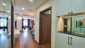 A modern hotel corridor with wooden flooring, a dining area with chairs and tables, and a kitchenette with cabinets and a countertop. - Asahi Luxstay - Golden Park  Apartments (Hanoi)