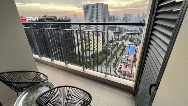 A balcony with a view of a cityscape during sunset, featuring modern buildings and a Ferris wheel. - Asahi Luxstay - Golden Park  Apartments (Hanoi)