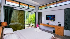 A modern hotel room with a large bed, a desk with a computer monitor, and a sliding glass door to the outside. - ProudChan Boutique Resort (Chanthaburi)