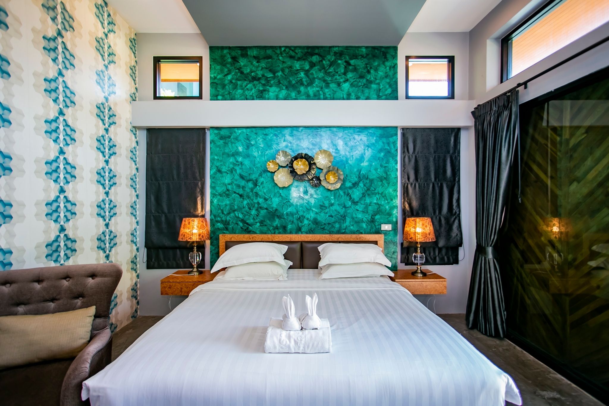 Quarto de hotel com uma cama grande, duas mesas de cabeceira com abajures, um painel de cabeceira, um detalhe decorativo na parede e vista para o exterior.