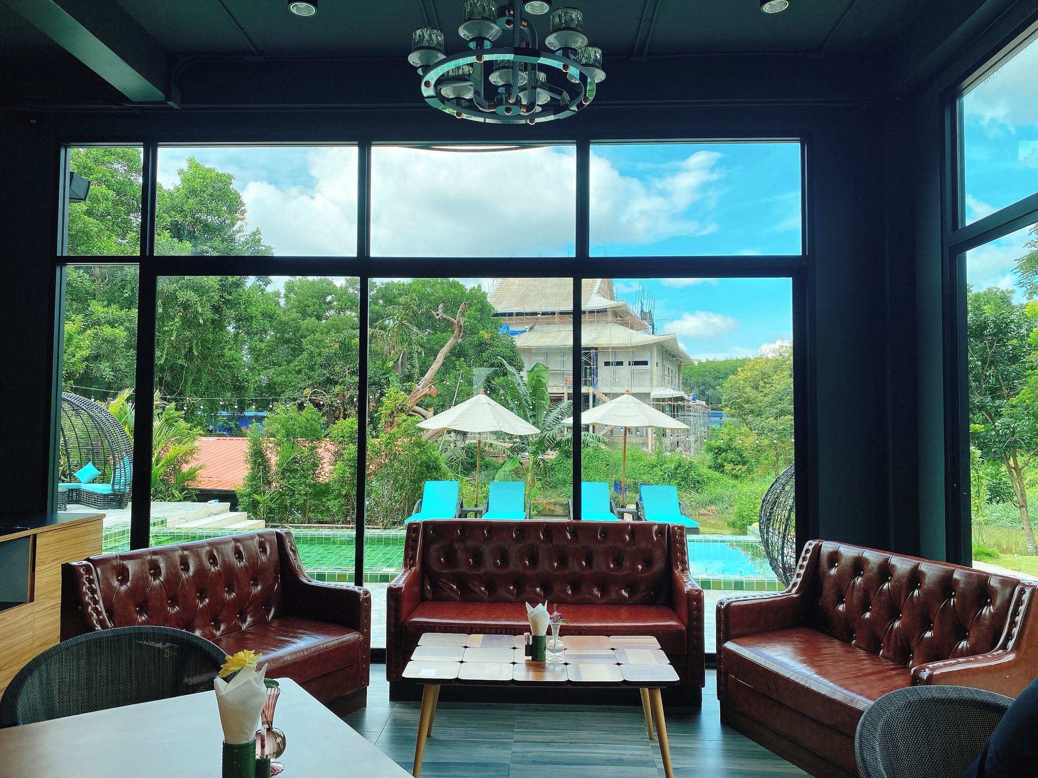 A room with leather sofas, a coffee table, and large windows overlooking a pool and greenery.