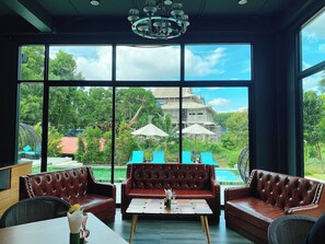 A room with leather sofas, a coffee table, and large windows overlooking a pool and greenery. - ProudChan Boutique Resort (Chanthaburi)