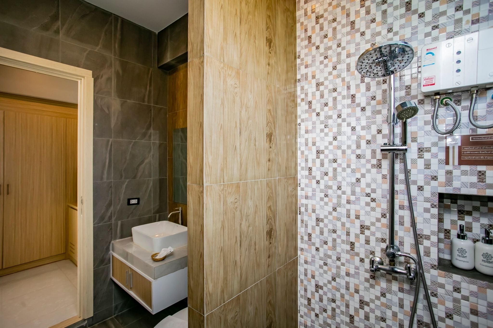 Un baño con tocador de madera, ducha con cabezal de lluvia y pared revestida con un diseño geométrico.