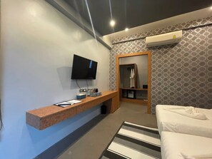 A modern hotel room with a flat-screen TV mounted on the wall, a wooden console table with a flat-screen TV, a built-in closet, and a striped area rug. - ProudChan Boutique Resort (Chanthaburi)