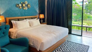 A bedroom with a large bed, a blue wall, and a view of a garden through a sliding door. - ProudChan Boutique Resort (Chanthaburi)