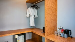 A hotel room with a wooden desk, a hanging robe, a small fridge, and a coffee station. - ProudChan Boutique Resort (Chanthaburi)