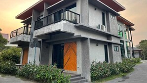 Une maison moderne à deux étages, dotée d’un toit plat, d’une façade en béton et d’un balcon à l’étage supérieur.