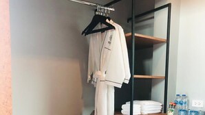 A compact hotel room with a wooden desk, a mirror, a small refrigerator, a shelf with toiletries, and a pair of slippers. - ProudChan Boutique Resort (Chanthaburi)