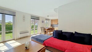 A modern room with a large sliding glass door leading to a garden, a dining area, and a kitchenette.