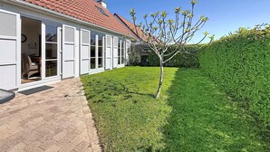 A house with a red-tiled roof, a white exterior, and a small tree in the yard.