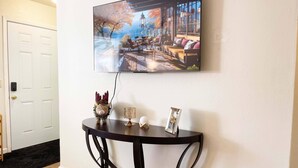 A room with a TV mounted on the wall displaying a scenic view, a small table with decorative items, and a door with a doorknob.