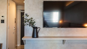 A modern interior with a flat-screen TV mounted on a wall, a wooden console table, and a potted plant. - Apartment Hotel 11 Umeda (Osaka)