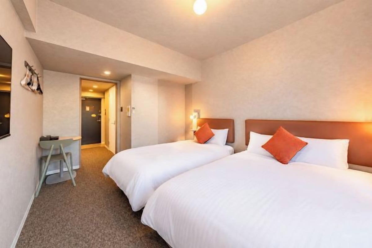 A hotel room with two beds, a desk, and a chair.