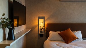 A modern bedroom with a bed, pillows, a nightstand, a wall-mounted TV, and a wall-mounted light fixture. - Apartment Hotel 11 Umeda (Osaka)