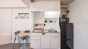A compact kitchen with a sink, a microwave, a refrigerator, and a dining area with a chair and table.