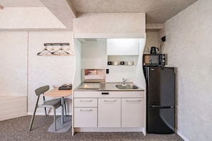 A compact kitchen with a sink, a microwave, a refrigerator, and a dining area with a chair and table.