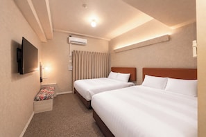 A hotel room with two beds, a flat-screen TV, an air conditioning unit, and a small seating area with a floral cushion.