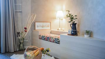 A neatly arranged hotel room with a bed, a bedside table with a lamp, a small potted plant, and a wicker basket on the floor.