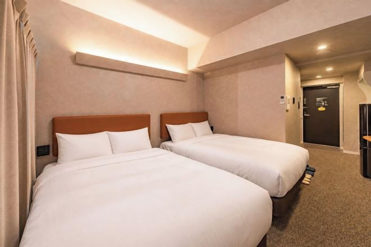 A hotel room with two beds, a carpeted floor, and a door leading to a bathroom.
