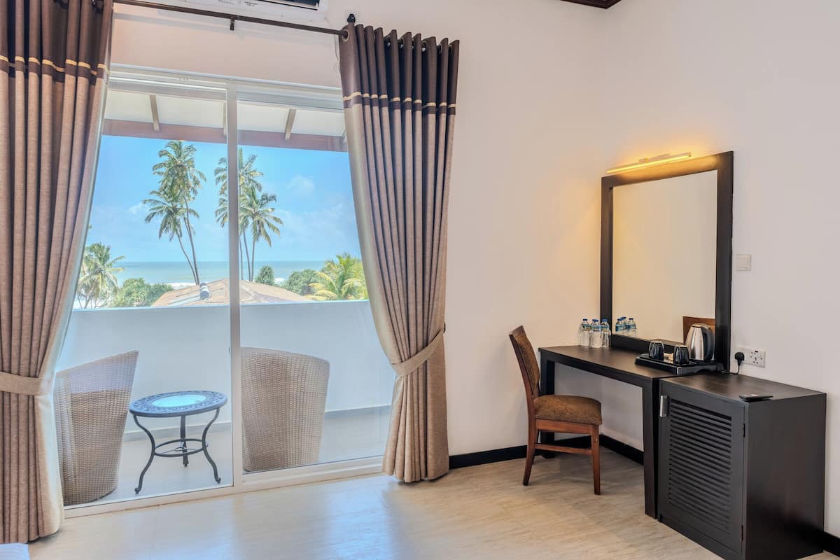 A room with a balcony, a desk, a chair, and a small table.