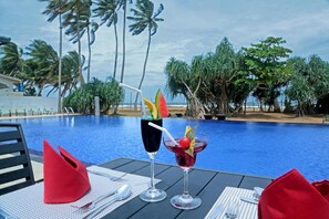 A poolside table with two drinks, a red napkin, and a white napkin. - Rathna Beach Wadduwa (Wadduwa)