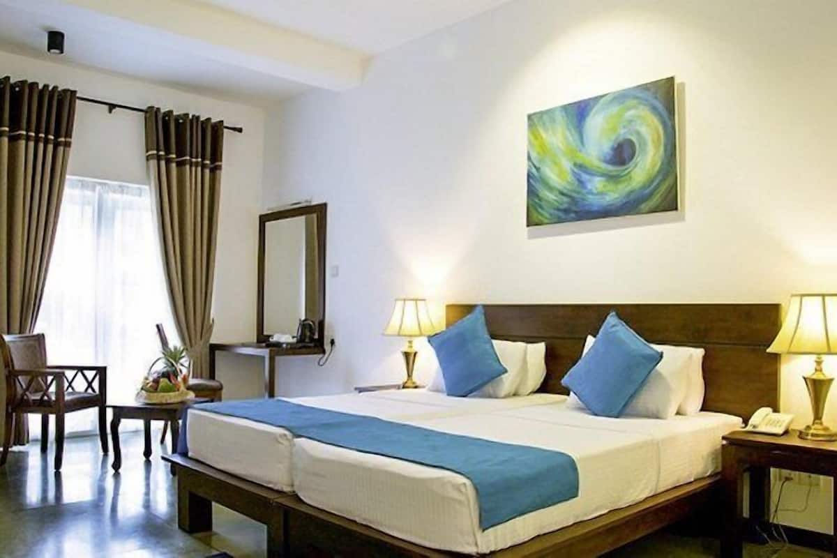 A hotel room with a large bed, two bedside lamps, a desk with a telephone, a chair, a mirror, and a painting on the wall.