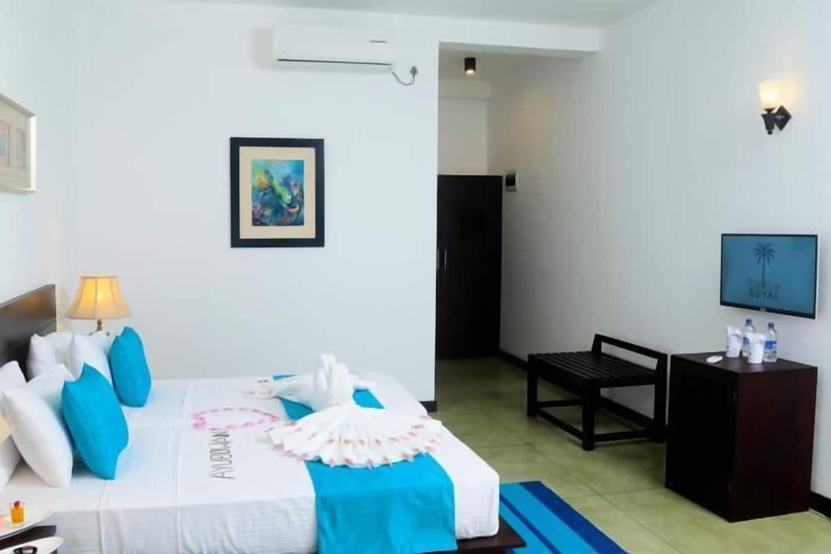 A hotel room with a bed, bedside lamps, a TV, a desk with water bottles, and a framed picture on the wall.