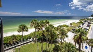 A beach view with palm trees, a parking area, and a clear sky. - Island Living! Beachfront Condo. Local Art. Heated Pool, Tennis, Spacious, Private & Secure. (Treasure Island)