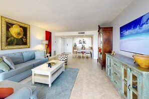Una sala de estar con sofá, mesa de centro y televisor. Hay un comedor con mesa y sillas.