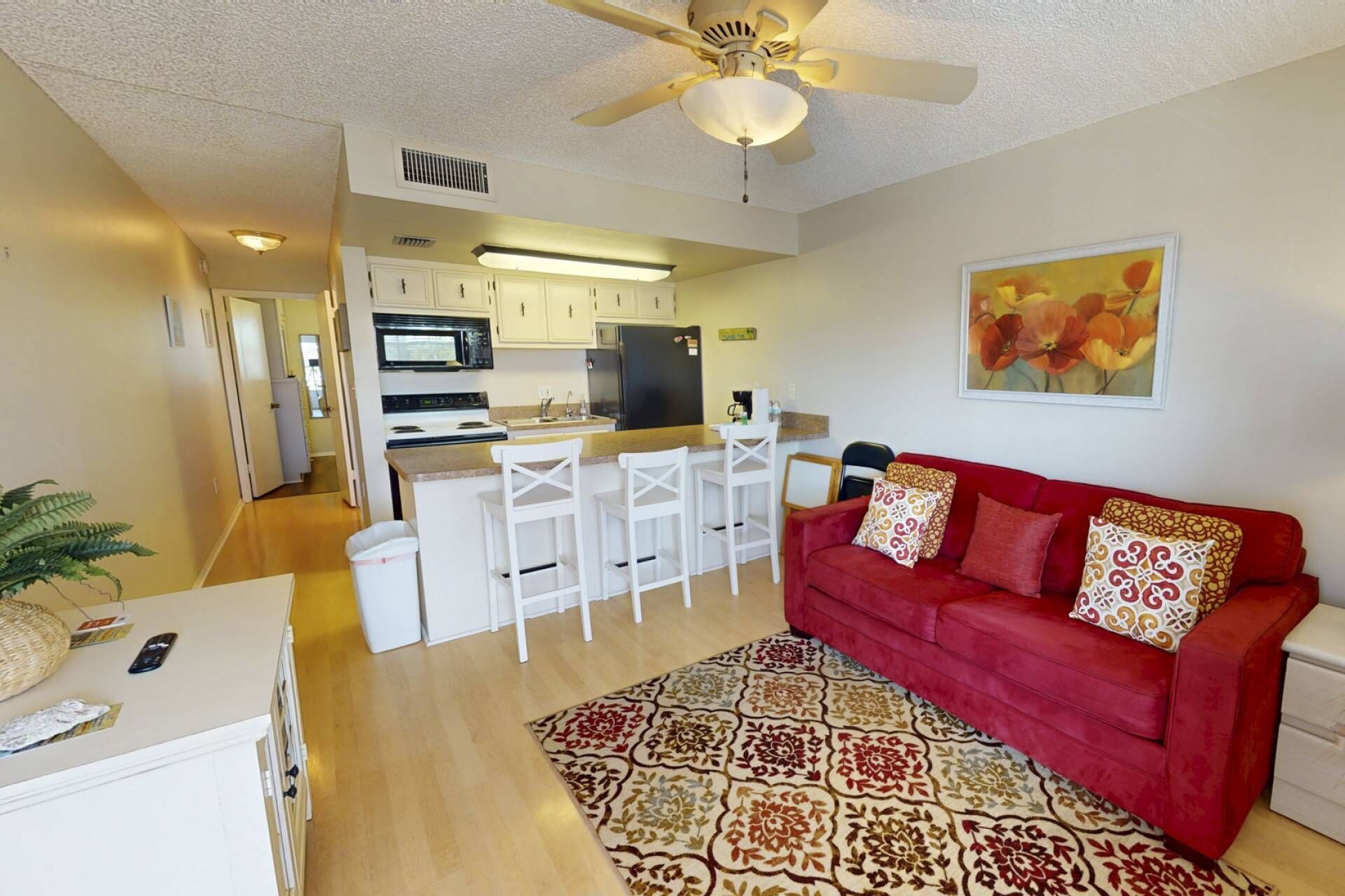 Un espacio habitable pequeño con kitchenette, un sofá rojo y un tapete estampado.