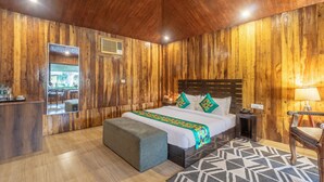 A wooden-paneled room with a bed, a bench, a nightstand, and a lamp. - Treebo Tiger Pug Mark Resort with Pool (Kaladhungi)