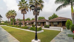 A resort with thatched-roof cottages, a well-maintained lawn, and a central street lamp. - Treebo Tiger Pug Mark Resort with Pool (Kaladhungi)