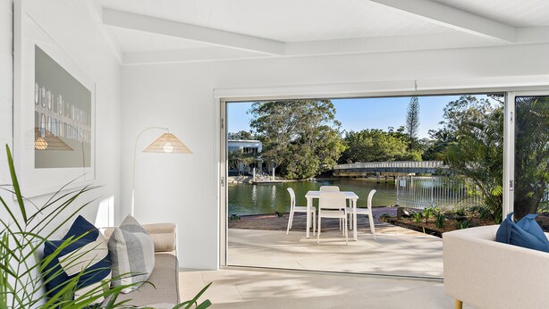 A modern living room with a glass door leading to an outdoor patio with a pool and greenery. - Edgewater Collection by Stay Noosa (Noosa Heads)
