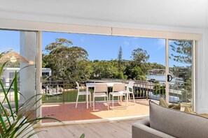 A balcony with a table and chairs, a view of a pool, and a large window. - Edgewater Collection by Stay Noosa (Noosa Heads)