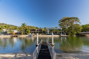 A waterfront hotel with a dock leading to the water, surrounded by palm trees and a clear blue sky. - Edgewater Collection by Stay Noosa (Noosa Heads)