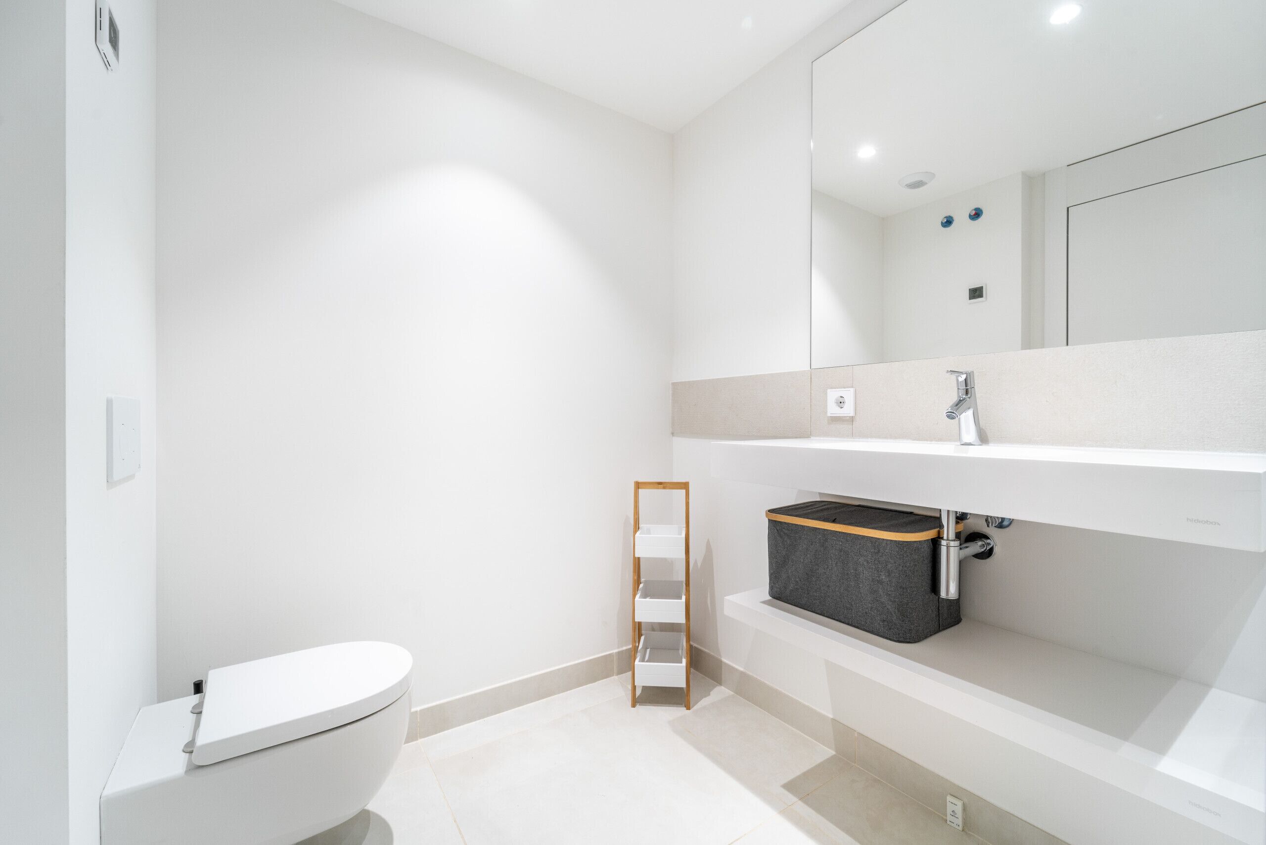 A modern bathroom with a toilet, a wooden shelf, and a grey storage bin under the sink.